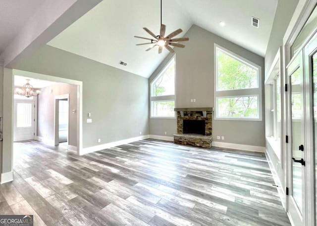 unfurnished living room featuring ceiling fan with notable chandelier, light hardwood / wood-style floors, a stone fireplace, and high vaulted ceiling