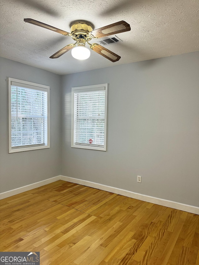 empty room featuring ceiling fan, plenty of natural light, light hardwood / wood-style floors, and a textured ceiling