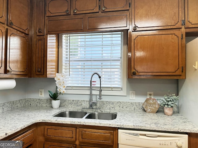 kitchen with light stone countertops, white dishwasher, and sink