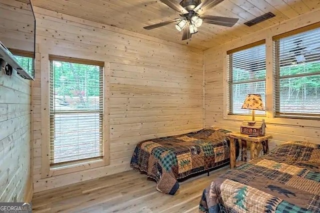 bedroom with ceiling fan, wooden ceiling, light hardwood / wood-style flooring, and wooden walls