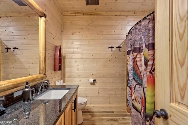 bathroom with toilet, vanity, and wood walls