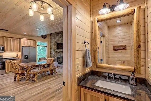 bathroom with hardwood / wood-style floors, wood ceiling, vanity, a fireplace, and wood walls