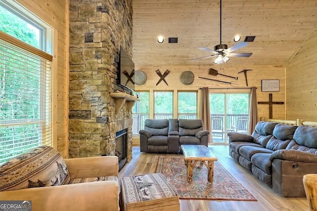 living room with a fireplace, light hardwood / wood-style floors, ceiling fan, wooden walls, and high vaulted ceiling