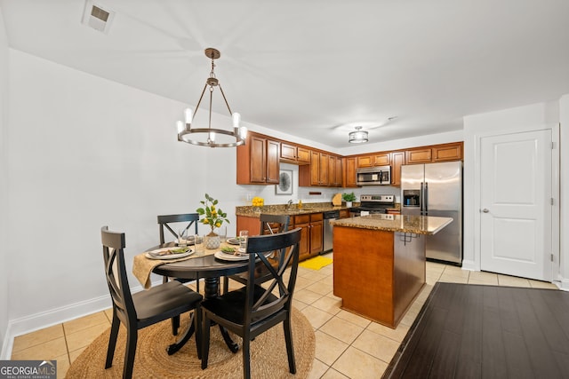 kitchen with hanging light fixtures, stainless steel appliances, light tile patterned floors, dark stone countertops, and a kitchen island