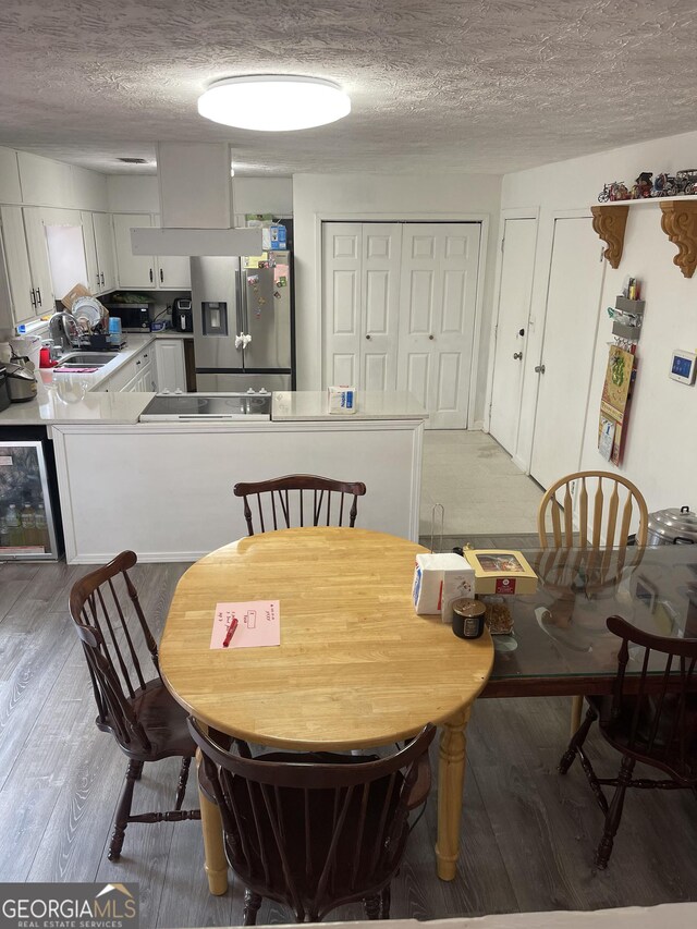 dining room featuring sink, a textured ceiling, beverage cooler, and light hardwood / wood-style flooring