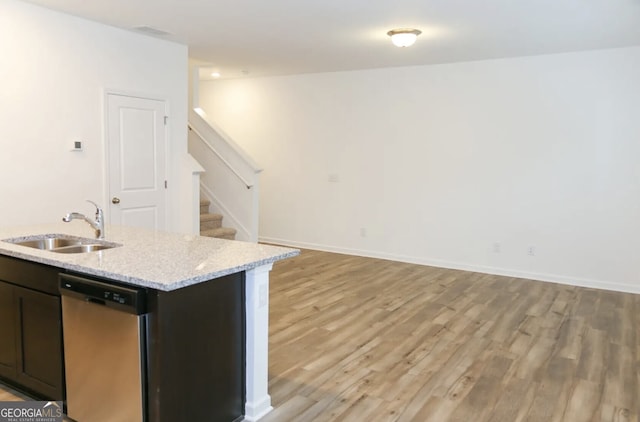 kitchen featuring an island with sink, sink, stainless steel dishwasher, light stone counters, and light wood-type flooring