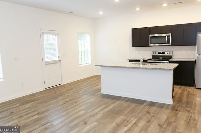 kitchen with an island with sink, appliances with stainless steel finishes, sink, and backsplash