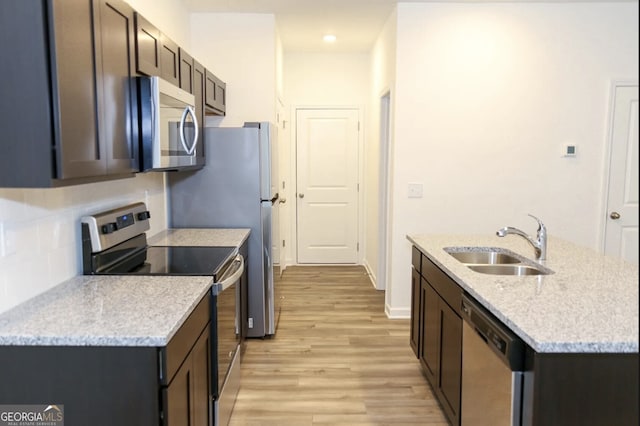 kitchen featuring sink, dark brown cabinetry, stainless steel appliances, light stone countertops, and light hardwood / wood-style flooring