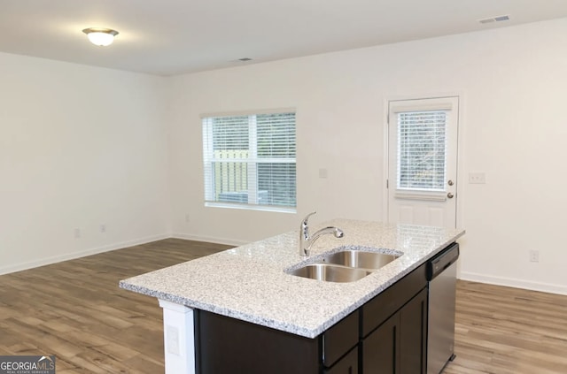 kitchen featuring dishwasher, sink, light stone countertops, dark brown cabinets, and a center island with sink