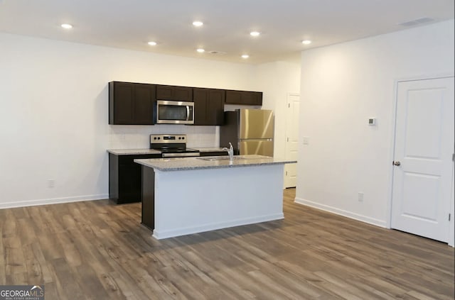 kitchen with sink, hardwood / wood-style flooring, appliances with stainless steel finishes, tasteful backsplash, and a center island with sink