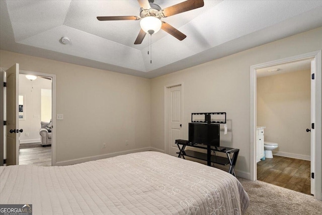 bedroom featuring a tray ceiling, ensuite bath, and ceiling fan