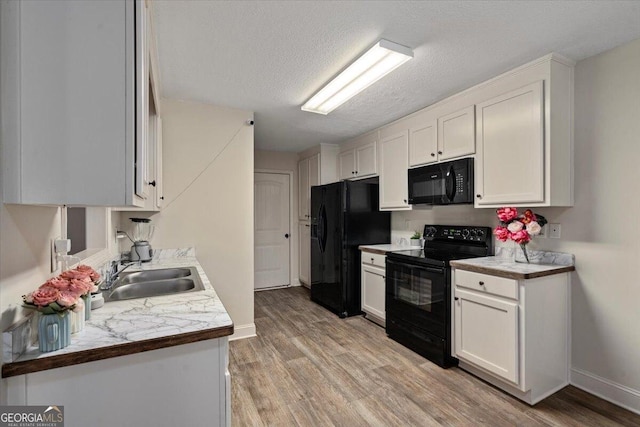 kitchen with a textured ceiling, sink, black appliances, white cabinets, and light hardwood / wood-style floors