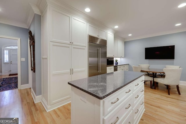 kitchen featuring built in fridge, crown molding, dark stone counters, light hardwood / wood-style floors, and white cabinets