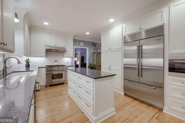 kitchen with dark stone countertops, white cabinetry, sink, and premium appliances