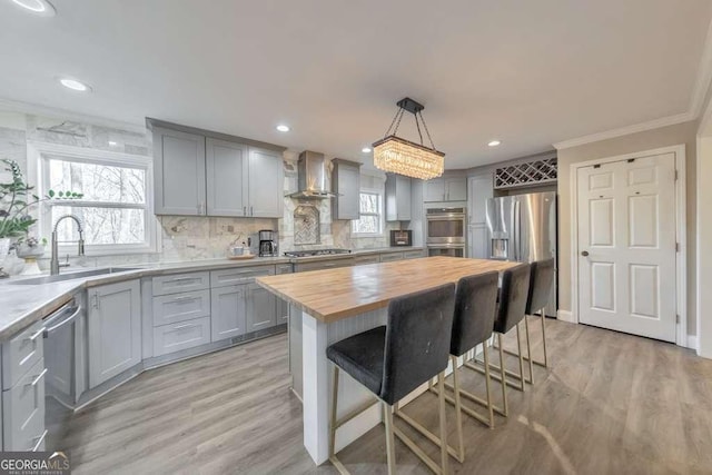 kitchen featuring pendant lighting, appliances with stainless steel finishes, a center island, wall chimney range hood, and butcher block countertops