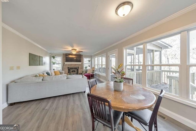 dining area with light hardwood / wood-style floors, a brick fireplace, ornamental molding, and ceiling fan