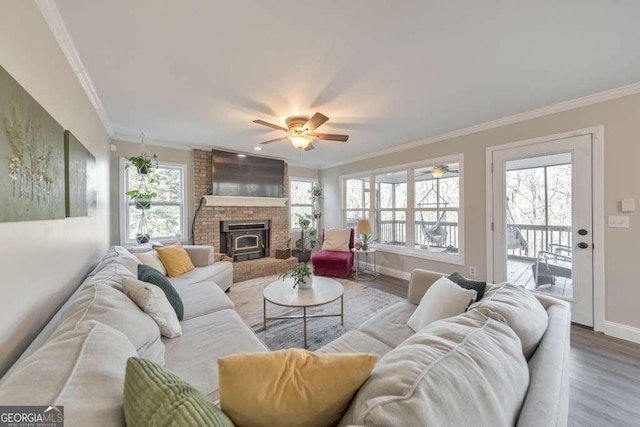 living room with ceiling fan, a wood stove, wood-type flooring, and ornamental molding