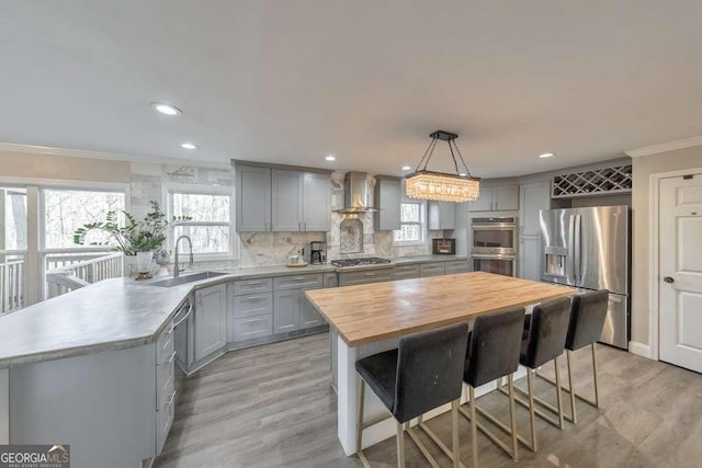 kitchen featuring decorative light fixtures, wall chimney range hood, a kitchen island, sink, and appliances with stainless steel finishes