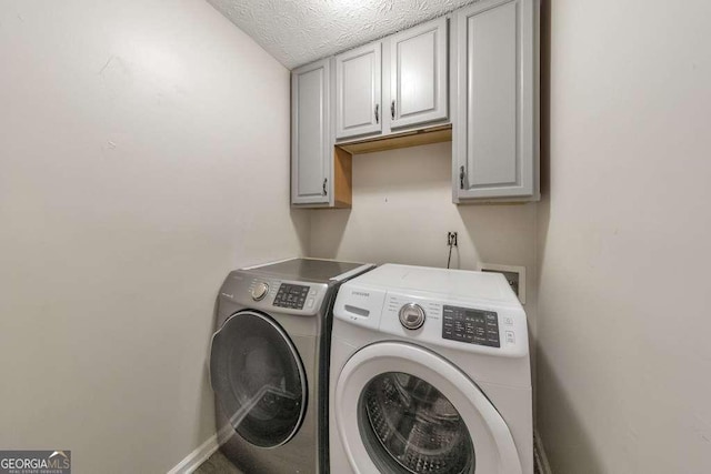 clothes washing area featuring a textured ceiling, cabinets, and washer and dryer