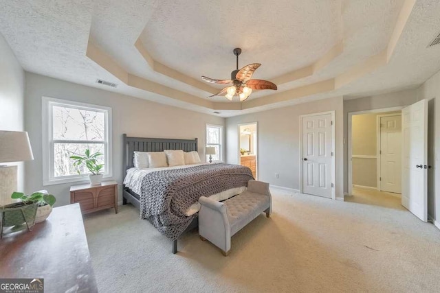 bedroom with a raised ceiling, light colored carpet, ceiling fan, and a textured ceiling