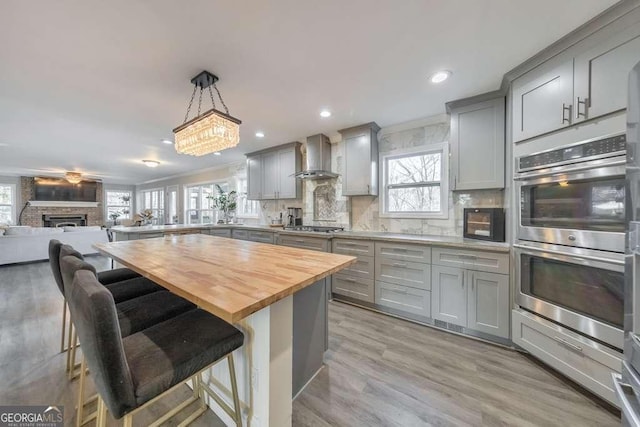 kitchen featuring gray cabinetry, wall chimney exhaust hood, a kitchen bar, and butcher block countertops