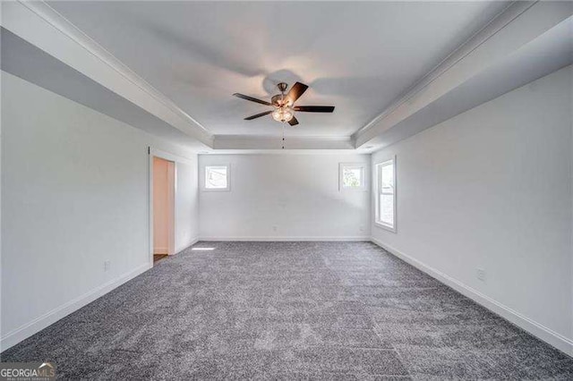 empty room with a raised ceiling, ceiling fan, dark carpet, and ornamental molding