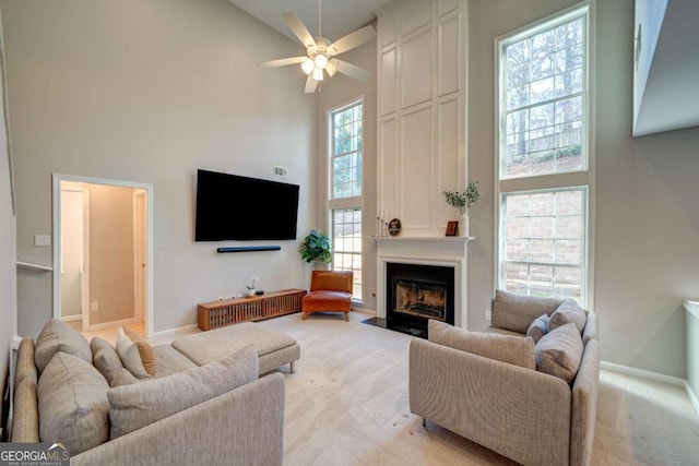 living room featuring a fireplace, a towering ceiling, light colored carpet, and ceiling fan