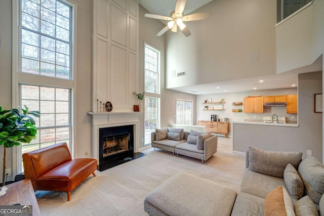 living room with ceiling fan, a large fireplace, a towering ceiling, and a healthy amount of sunlight