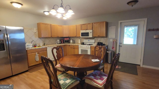 kitchen featuring a chandelier, pendant lighting, white appliances, light hardwood / wood-style floors, and decorative backsplash