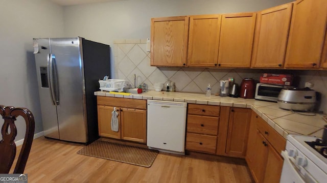 kitchen featuring decorative backsplash, light wood-type flooring, white appliances, and tile countertops