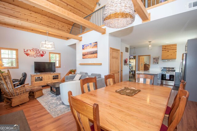 dining area featuring a chandelier, a high ceiling, light hardwood / wood-style flooring, and beam ceiling