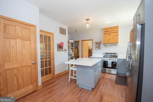 kitchen featuring gray cabinetry, stainless steel appliances, light hardwood / wood-style floors, decorative light fixtures, and a breakfast bar