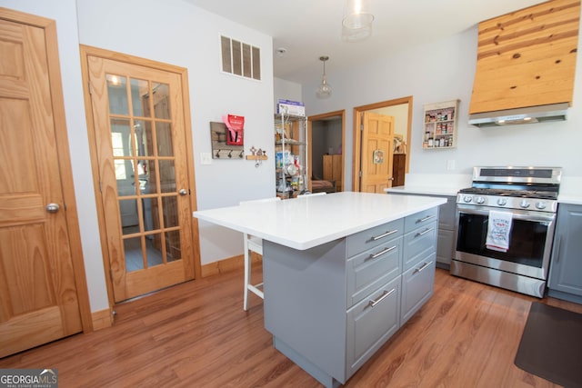 kitchen with pendant lighting, gray cabinetry, ventilation hood, gas range, and a kitchen island