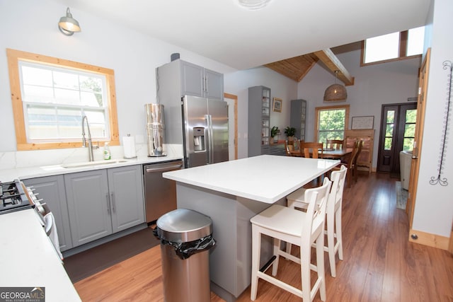 kitchen with gray cabinetry, sink, lofted ceiling with beams, a kitchen island, and appliances with stainless steel finishes