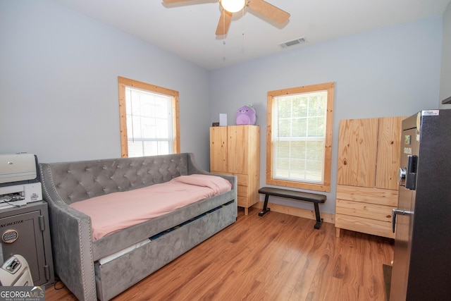 bedroom with black fridge, hardwood / wood-style floors, and ceiling fan