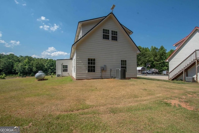 rear view of house with central air condition unit and a lawn