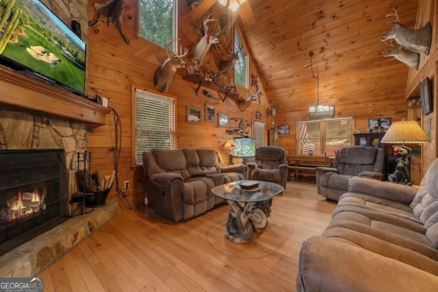 living room with ceiling fan, wooden walls, light hardwood / wood-style flooring, high vaulted ceiling, and a fireplace