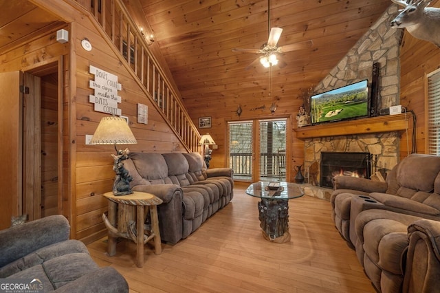 living room with ceiling fan, wooden walls, wooden ceiling, light hardwood / wood-style floors, and a stone fireplace