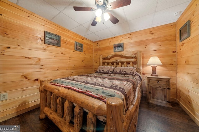 bedroom featuring ceiling fan, wood walls, and dark hardwood / wood-style flooring