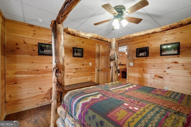 bedroom with a paneled ceiling, ceiling fan, and wooden walls