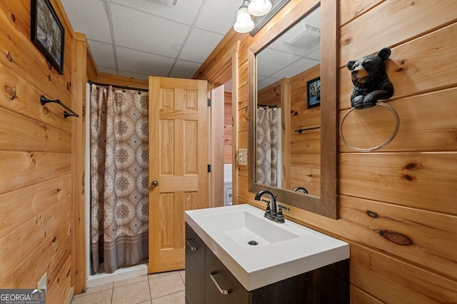 bathroom with walk in shower, tile patterned flooring, a paneled ceiling, wooden walls, and vanity