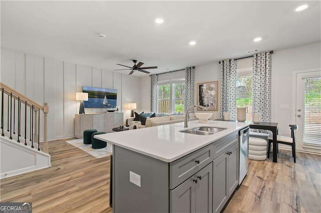 kitchen featuring stainless steel dishwasher, gray cabinetry, ceiling fan, a center island with sink, and light hardwood / wood-style flooring