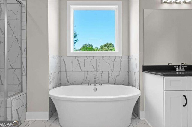 bathroom with marble finish floor, a freestanding tub, and vanity