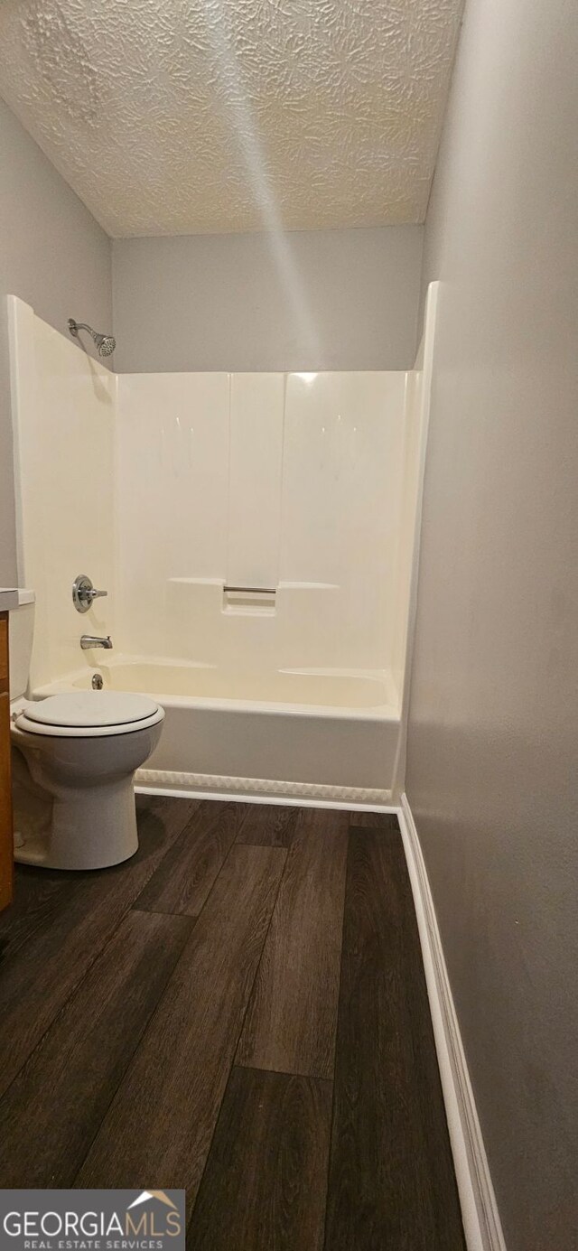 full bathroom featuring hardwood / wood-style floors, vanity,  shower combination, toilet, and a textured ceiling