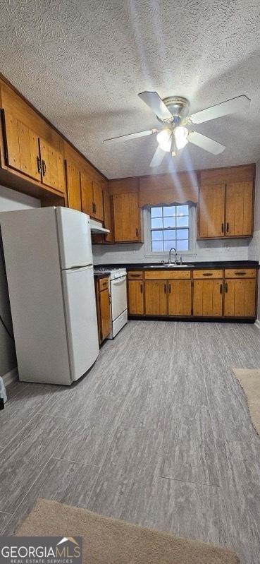 kitchen with ceiling fan, sink, white fridge, a textured ceiling, and range