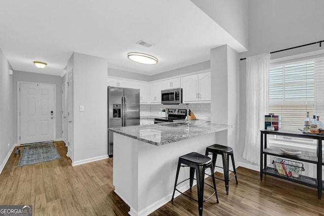 kitchen featuring decorative backsplash, appliances with stainless steel finishes, light wood-type flooring, light stone counters, and white cabinets