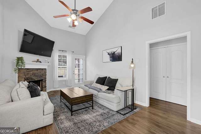 living room with ceiling fan, dark hardwood / wood-style flooring, a stone fireplace, and high vaulted ceiling