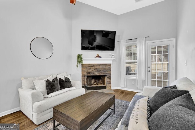 living room with a stone fireplace, hardwood / wood-style floors, and vaulted ceiling