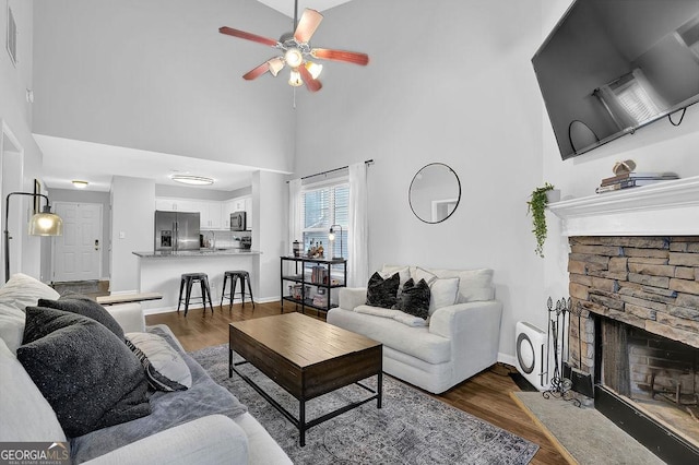 living room with ceiling fan, a fireplace, high vaulted ceiling, and dark wood-type flooring