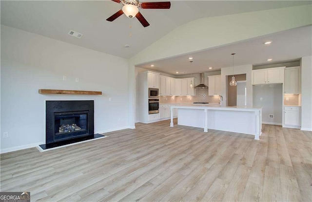 kitchen featuring white cabinets, wall chimney exhaust hood, a kitchen island with sink, and appliances with stainless steel finishes